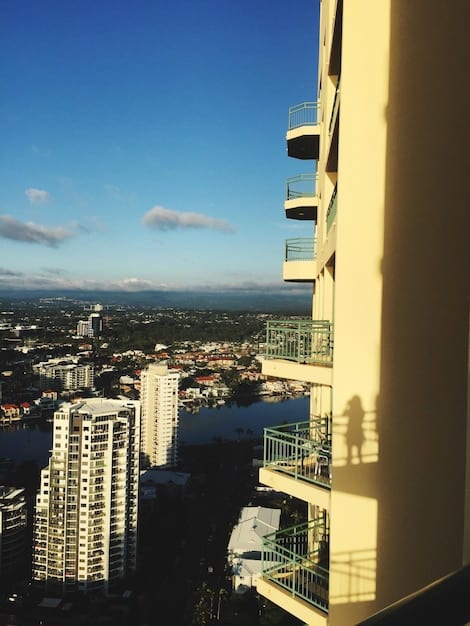 A photograph of a modern residential building under a sunny sky, with a small business district in the background indicating mixed-use real estate opportunities.